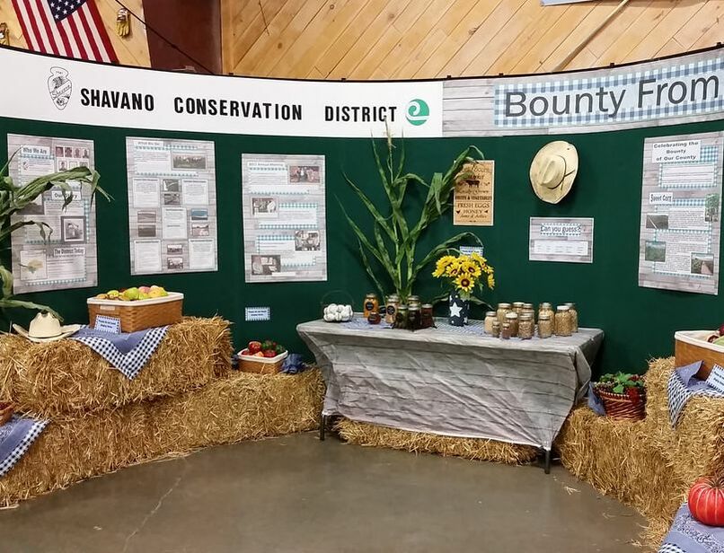 SCD information booth at Montrose County Fair displaying various seeds, corn stalks, straw bales, and fruits and veggies grown in Montrose County