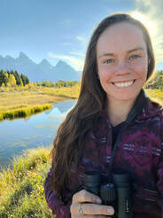 Cassie holding binoculars, and lake and mountain range behind her in the distance
